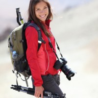 A beautiful female photographer holds a tripod and a DSLR while hiking and camping.