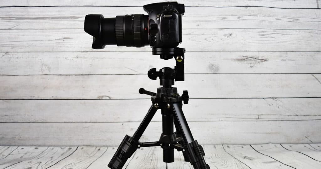 Digital camera with tripod on wooden background