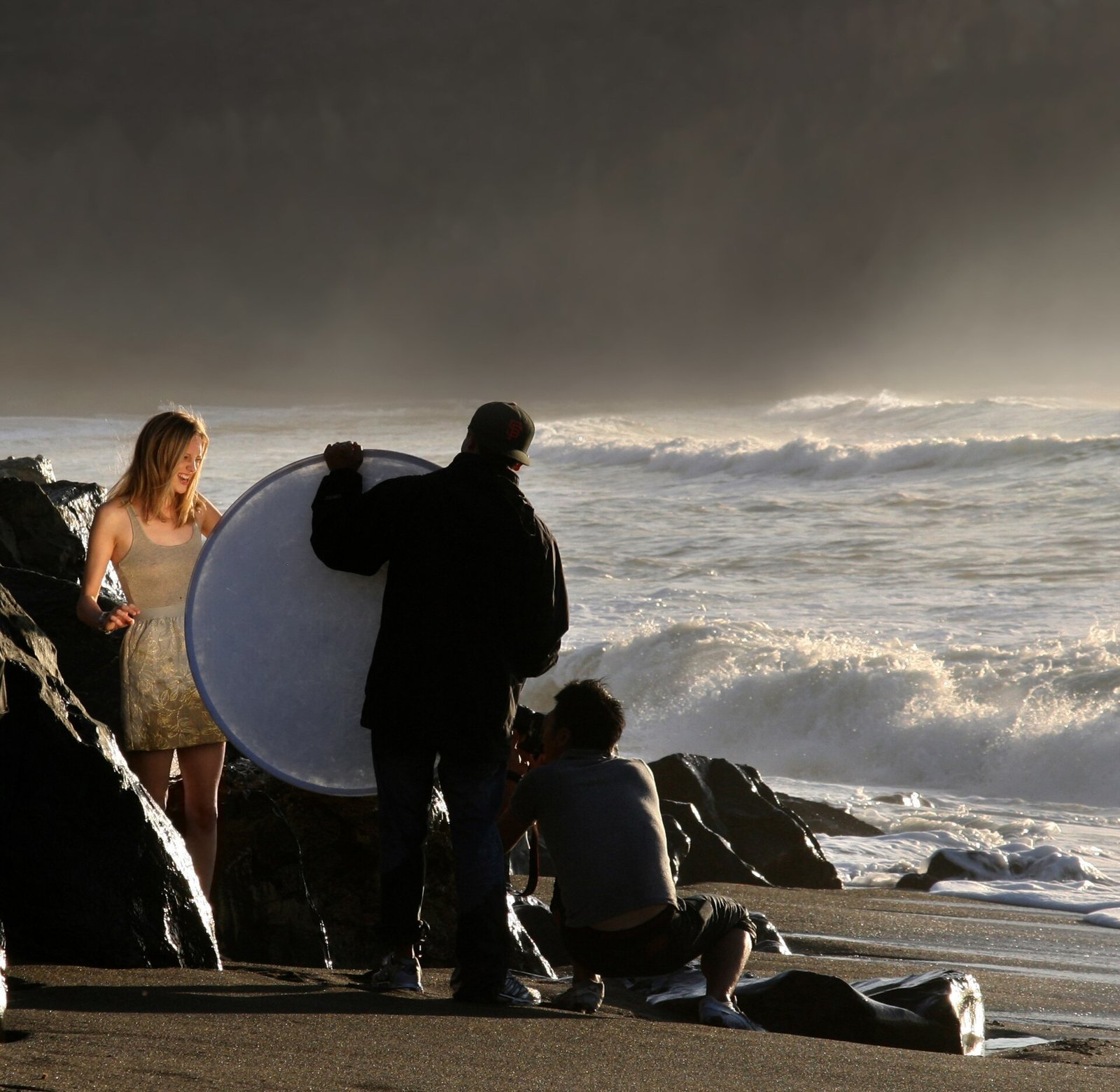 Photographer and assistant with a reflector shooting a model on a beach at golden hour