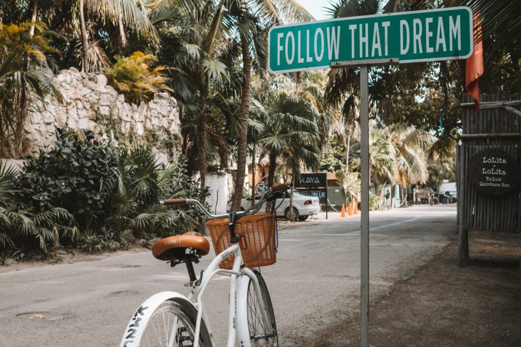 Bicycle parked beside a Follow That Dream street sign on a tropical road